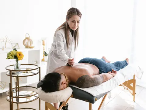 Practitioner in a white coat treating a man lying on a table in a bright treatment room