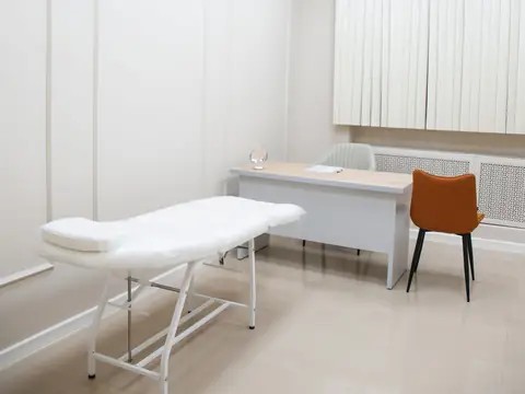 Bright white clinic room with a treatment couch, desk and chair