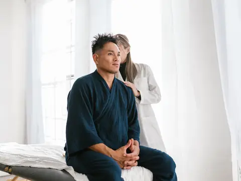 Clinician talking with a man seated on the edge of a treatment table in a bright room